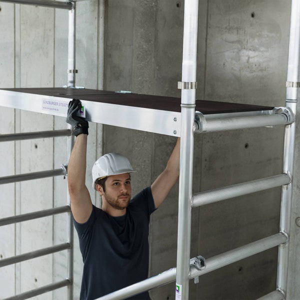 Mann montiert ein Gerüst mit einer Arbeitsplattform