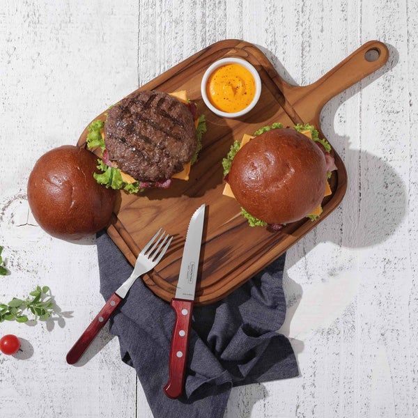 Zwei Burger auf einem Holzbrett mit Dip, Gabel und Messer