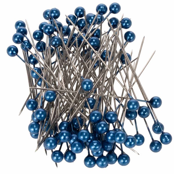 Tischgesteck mit weissen Ranunkeln und Vergissmeinnicht in einer runden Steckschaumform, dekoriert mit Schmucknadeln und Schleifen auf einem Tisch.