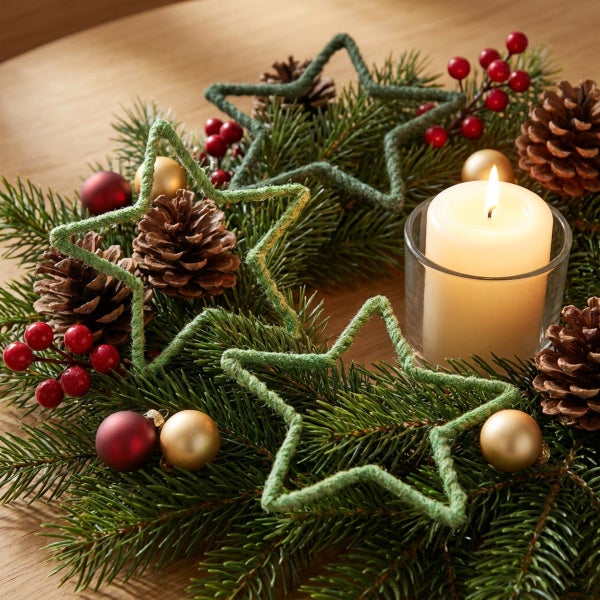 Weihnachtskranz aus Tannenzweigen mit Zapfen, Weihnachtskugeln, Beeren und Sternen sowie einer brennenden Kerze im Glas auf einem Holztisch.