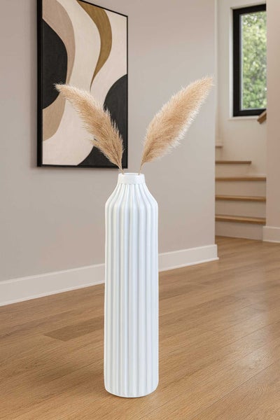 Hohe weiße Bodenvase mit geriffelter Struktur und Pampasgras in einem modern gestalteten Wohnraum mit hellem Holzboden.