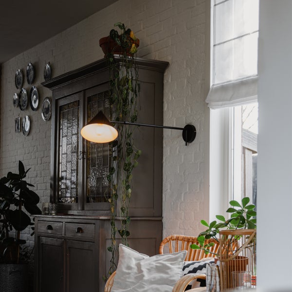 Wohnraum mit Schrank, Wandleuchte und Rattansessel