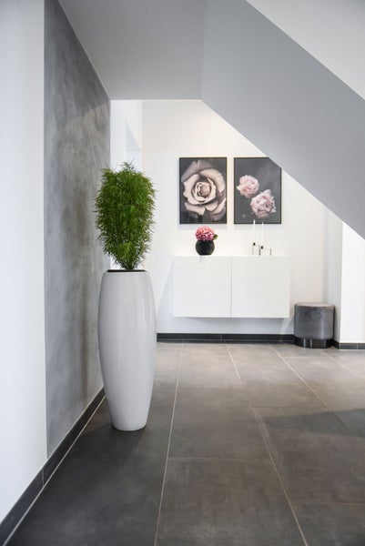 Moderner Flur mit hohem weißem Pflanzgefäß, grauen Bodenfliesen, schwebendem Sideboard und Wandbildern im hellen Design.