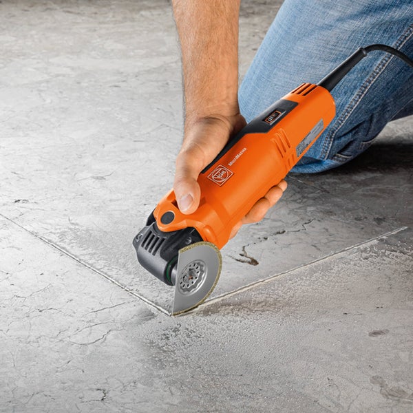 Ein Mann benutzt ein Multifunktionswerkzeug von Fein, um eine Fuge in einen Fliesenboden zu schneiden.