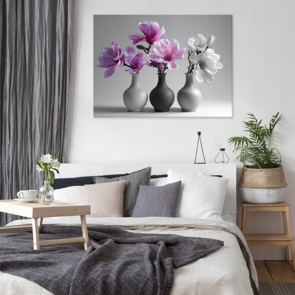 Wandbild mit Magnolien in Vasen über einem hellen Bett in einem modern gestalteten Schlafzimmer mit grauen und beigen Kissen und Decke.
