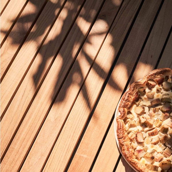 Helle Holzlatten eines Gartentisches mit einem Rhabarberkuchen und Blätterschatten.