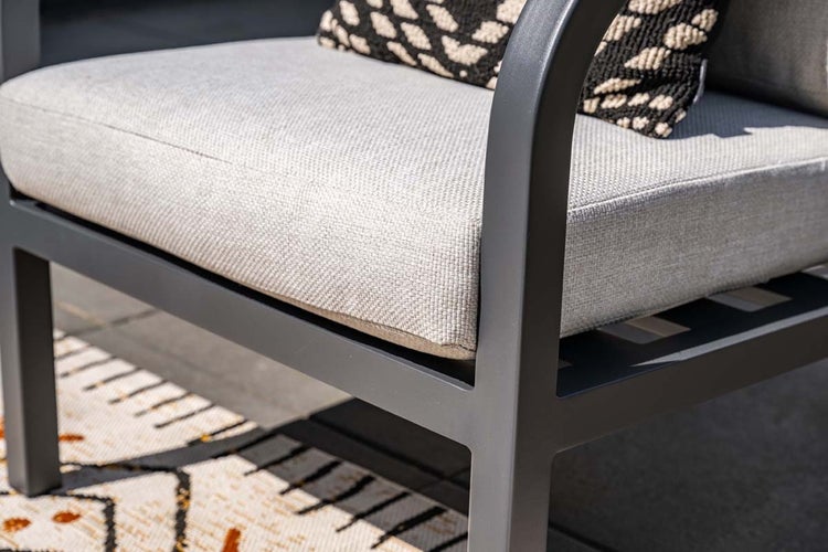Nahaufnahme eines Gartenstuhls mit einem dunklen Metallrahmen und einem dicken hellgrauen Sitzkissen.