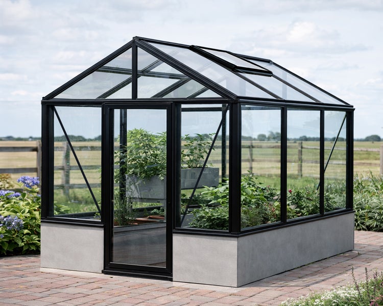 Modernes Gewächshaus mit schwarzem Aluminiumrahmen, Glasscheiben und einem hellgrauen Sockel in Betonoptik.