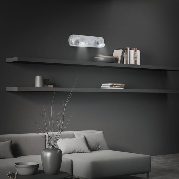 Modernes Wohnzimmer mit grauem Sofa, zwei Wandregalen und einer zweiflammigen Wandleuchte mit Bewegungsmelder über den Regalen.