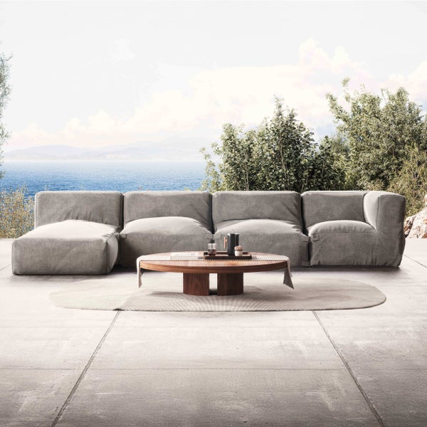 Moderne Outdoor-Lounge mit grauem Modulsofa, rundem Holztisch und hellem Teppich auf einer großzügigen Terrasse mit Blick auf das Meer.