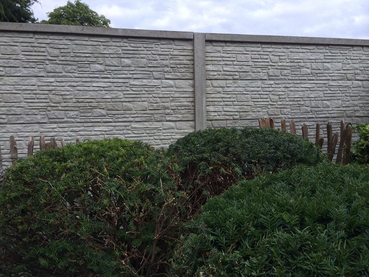 Betonzaun mit Steinmuster und grünen Büschen im Garten