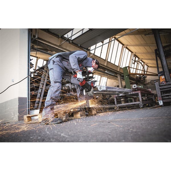 Handwerker mit Schutzkleidung und Schutzbrille nutzt einen Winkelschleifer, um Metall in einer Werkstatt zu bearbeiten, mit Funkenflug.