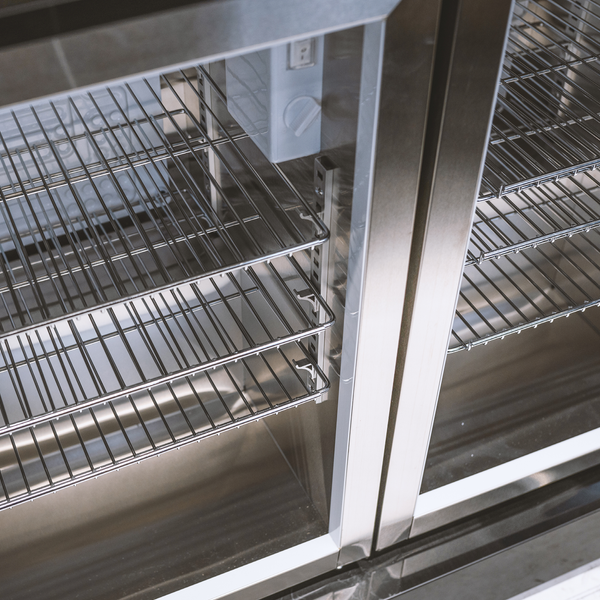 Innenansicht eines Kühlschranks aus Edelstahl mit verstellbaren Gitterrosten und Temperaturregler.