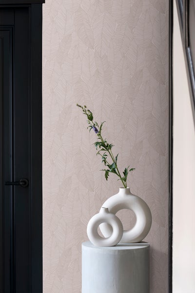 Nahaufnahme einer Wand mit Blattmuster-Tapete, einer dunklen Tür und dekorativen Vasen auf einem Podest