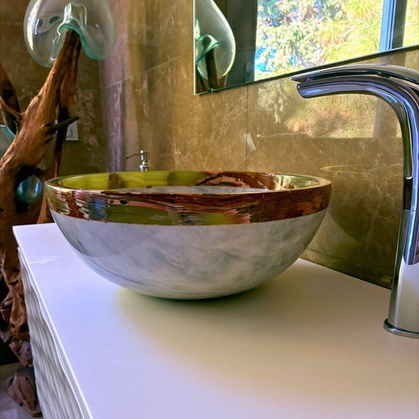 Rundes Aufsatzwaschbecken in Marmor-Optik mit gemustertem Rand auf weißem Waschtisch mit verchromter Armatur in einem modernen Badezimmer.