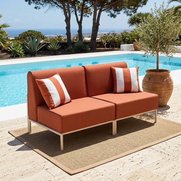 Modernes Zweisitzer-Gartensofa mit orangefarbenen Polstern und gestreiften Kissen auf einem Außenteppich an einem Pool mit Meerblick.