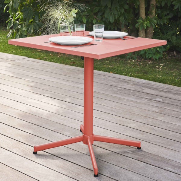 Quadratischer Bistrotisch aus Metall auf einer Holzterrasse, gedeckt mit Tellern und Gläsern.