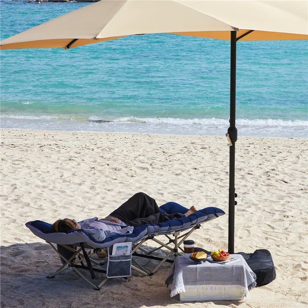 Strandszene mit Person auf einer gepolsterten Strandliege unter einem Sonnenschirm