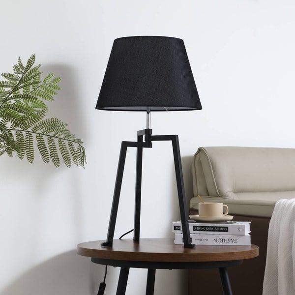 Tischleuchte mit schwarzem Lampenschirm und Stativfuß auf einem Beistelltisch