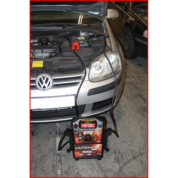 Auto mit Starthilfekabeln, die an einen Batterielader angeschlossen sind