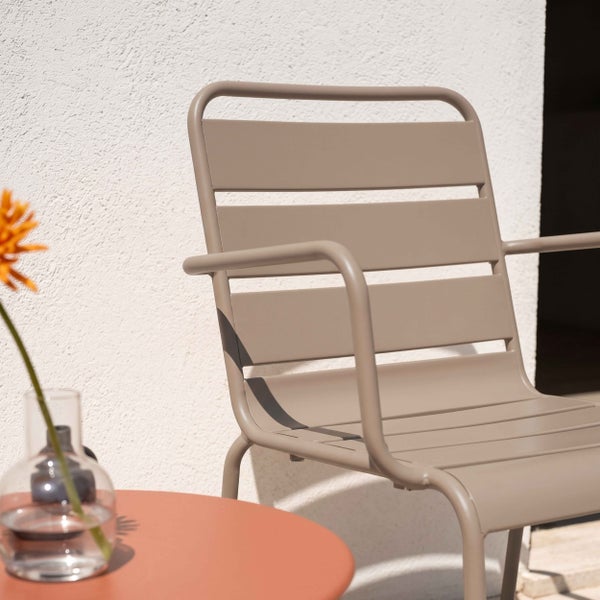 Moderner Gartenstuhl aus Metall in Taupe mit Armlehnen und Lamellen-Design neben einem Beistelltisch mit Vase.