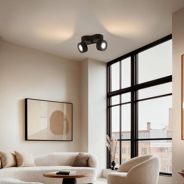 Zweiflammiger LED Deckenstrahler in Schwarz in einem hellen, modernen Wohnzimmer mit Sofa, Sessel und großem Fenster.
