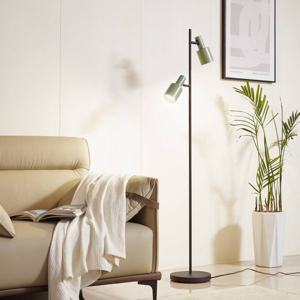 Stehleuchte mit zwei Leuchten in einem Wohnzimmer neben einer Couch und einer Pflanze.