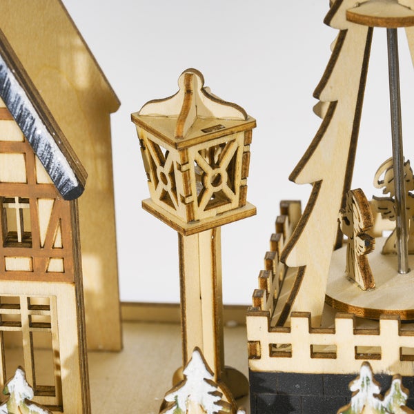 Detailansicht einer Weihnachtsdekoration aus Holz mit kleiner Straßenlaterne, Fachwerkhaus und Figuren eines Karussells.