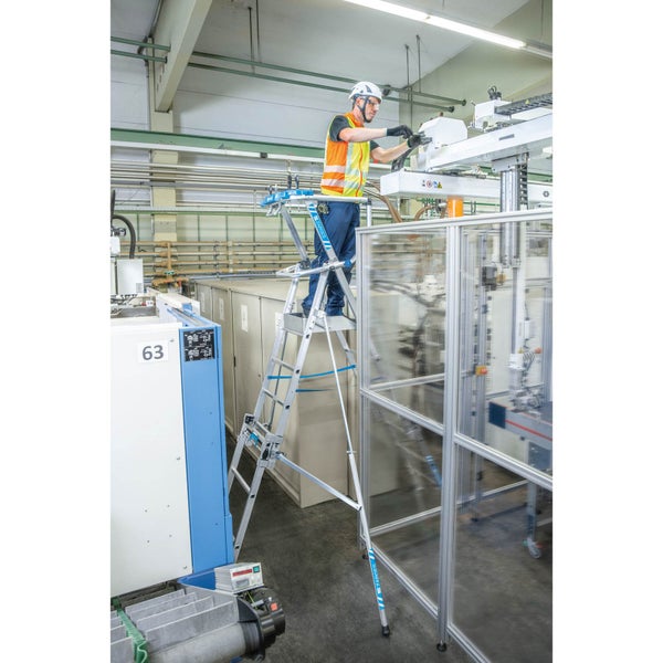 Mann in Arbeitskleidung auf einer Zarges Treppe in einer Produktionshalle bei Wartungsarbeiten an einer Maschine