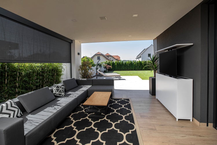 Moderne Terrasse mit grauer Couch, Couchtisch, schwarzem Teppich und Blick in den Garten