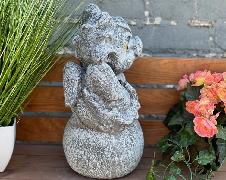 Gartenfigur kleiner Drache auf einer Kugel sitzend in Steinoptik, dekoriert mit Pflanzen auf einer Holzbank