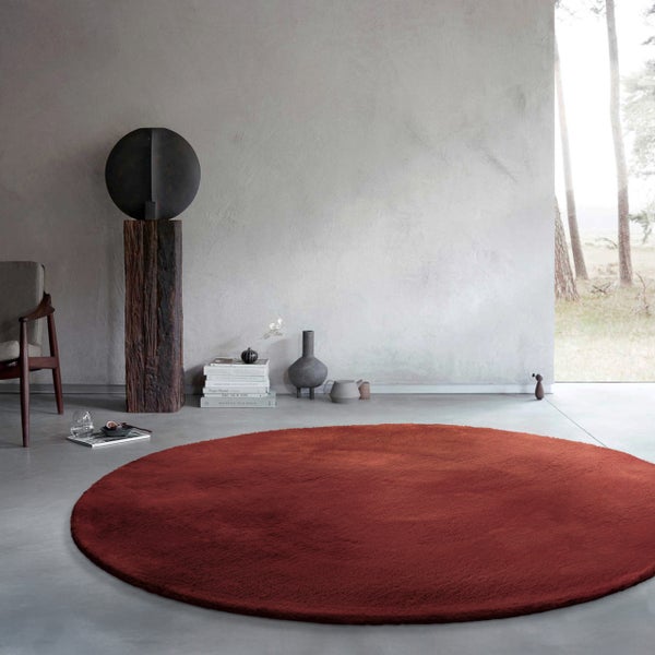 Runder Teppich in Terracotta in einem modernen Wohnraum mit Sichtbetonwänden und minimalistischer Dekoration.