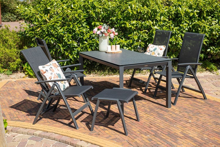 Modernes Gartenmöbel-Set aus Metall und Textilgewebe mit Tisch, Klappsesseln und Hocker auf einer gepflasterten Terrasse vor einer Hecke.