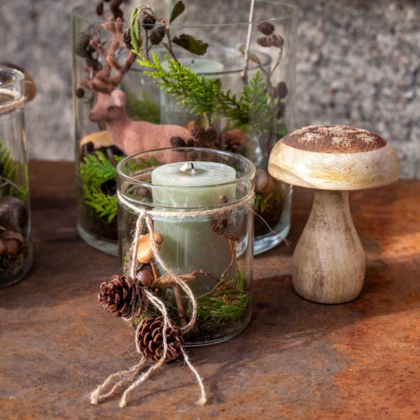 Dekorative Glasvasen mit Kerzen, Tannenzapfen, Moos und einer Hirschfigur für eine festliche Atmosphäre