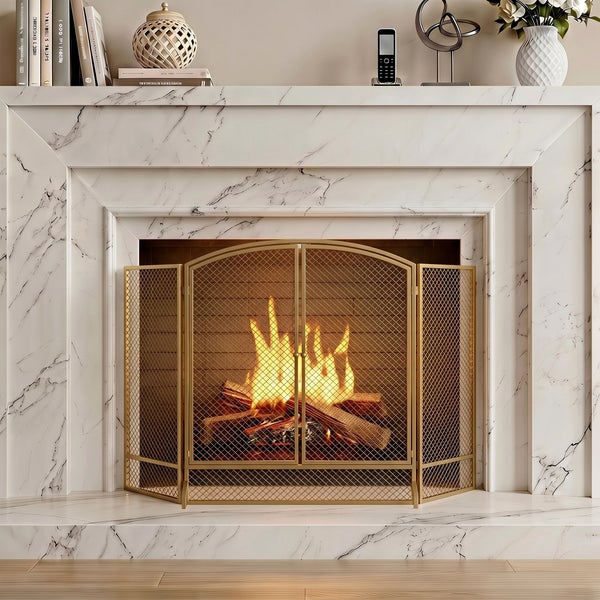 Goldener Funkenschutz vor einem Kamin mit brennendem Holzfeuer in einem Kamin aus weißem Marmor mit dekorativer Ablage.