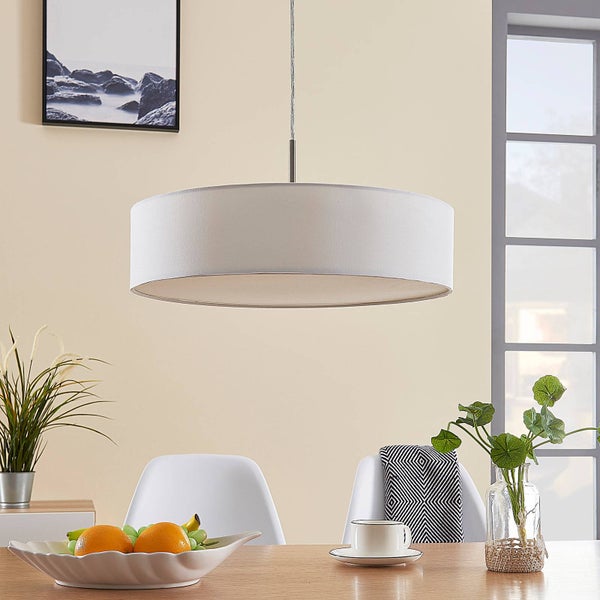 Weiße runde Pendelleuchte mit Textilschirm über einem Holztisch in einem hellen, modern eingerichteten Zimmer.