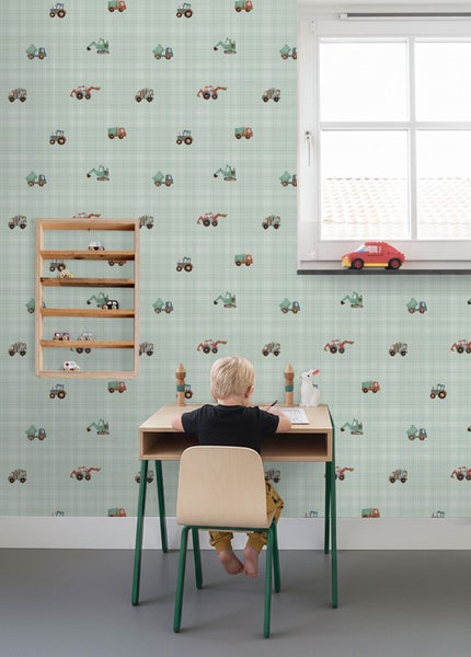 Kinderzimmer mit Tapete im Karomuster und Motiven von Baustellenfahrzeugen, ein Kind sitzt an einem Schreibtisch.