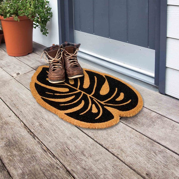 Fußmatte aus Kokosfaser mit Blattmuster vor einer Haustür mit Schuhen