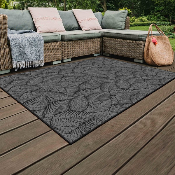 Outdoor-Teppich mit Blättermuster auf einer Holzterrasse vor einer Lounge-Sitzgruppe aus Polyrattan.