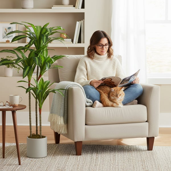 Helles Wohnzimmer mit Frau im Sessel, großer künstlicher Dracaena im Topf und Beistelltisch auf einem Teppich.