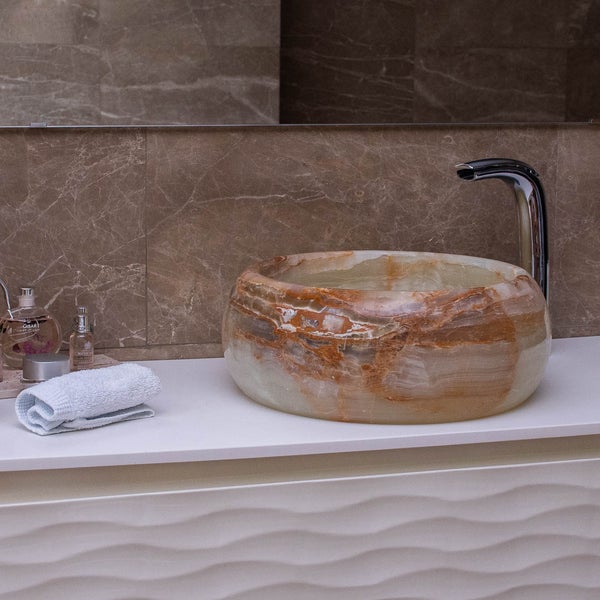 Rundes Aufsatzwaschbecken aus Naturstein mit Armatur auf einem weißen Unterschrank im modernen Badezimmer.