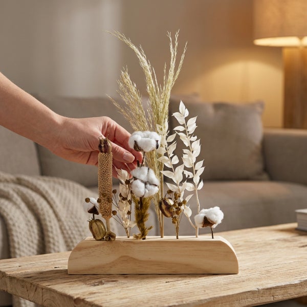 Tischdekoration aus Trockenblumen und Baumwollzweigen in einem Holzständer auf einem Holztisch.