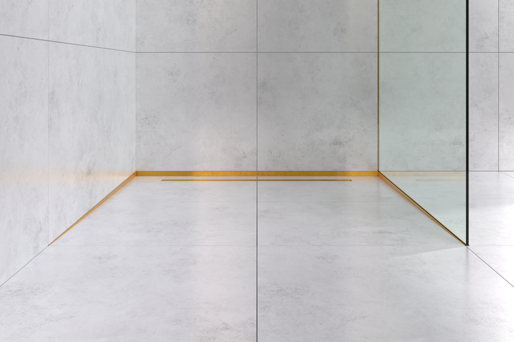Begehbare Dusche mit großformatigen Fliesen in Betonoptik, einer goldenen Duschrinne und einer Trennwand aus Glas.