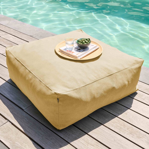 Quadratischer Outdoor-Pouf auf einer Holzterrasse am Pool, dekoriert mit einem Tablett, einem Glas, Snacks und Zeitschriften.