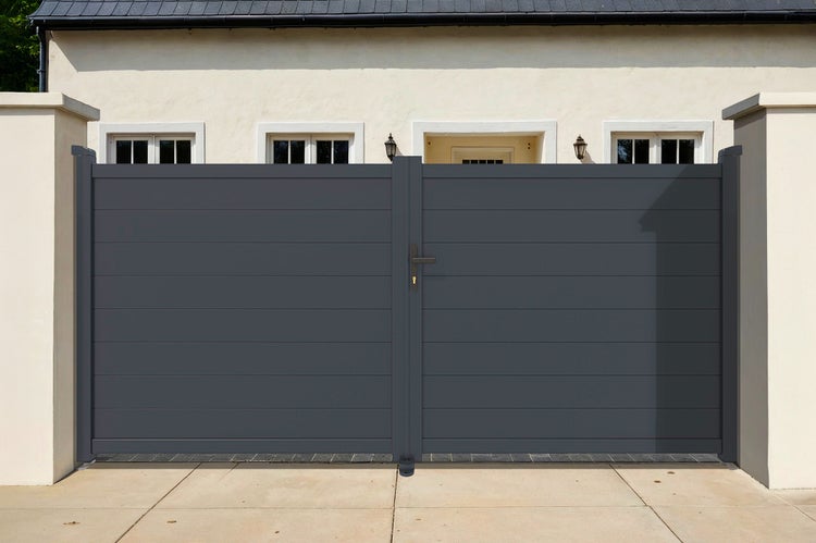 Modernes, blickdichtes Einfahrtstor aus anthrazitfarbenem Aluminium mit horizontalen Lamellen zwischen zwei hellen Pfeilern vor einem Wohnhaus.