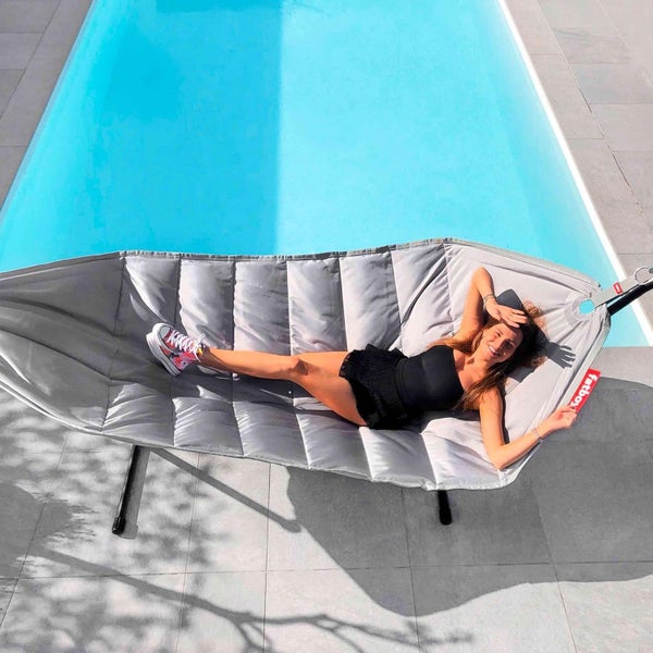 Frau entspannt in einer grauen Fatboy Hängematte neben einem Pool.