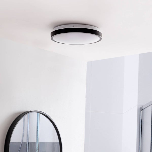 Moderne runde Deckenleuchte mit schwarzem Rand und weißem Diffusor in einem hellen Badezimmer mit weißen Fliesen und rundem Spiegel.