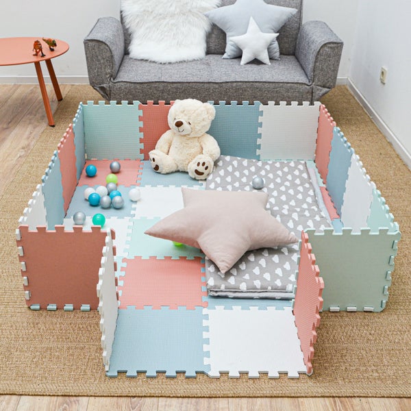 Schaumstoff-Puzzlematte als Spielbereich für Kinder mit weichen Bodenfliesen, Teddybär, Sternenkissen und Spielbällen in einem hellen Zimmer.