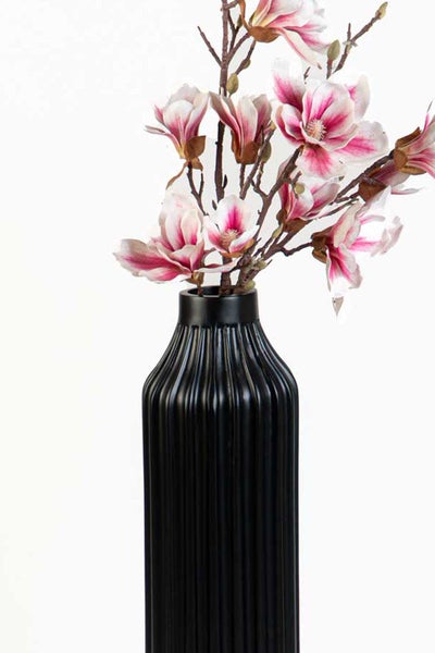 Schwarze Vase mit vertikaler Rillenstruktur und künstlichen Magnolienblüten in Rosa und Weiß.