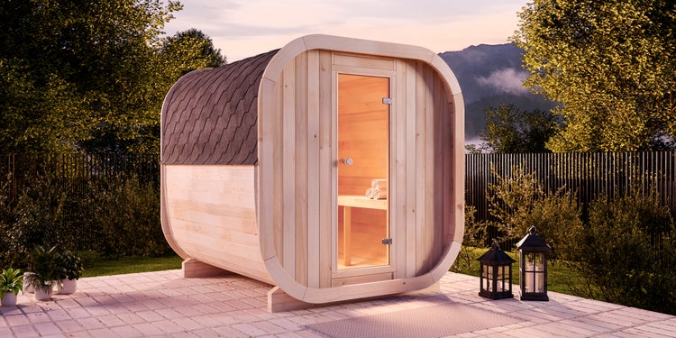 Fasssauna aus hellem Holz mit Glastür und Schindeldach im Außenbereich auf einer gepflasterten Terrasse.